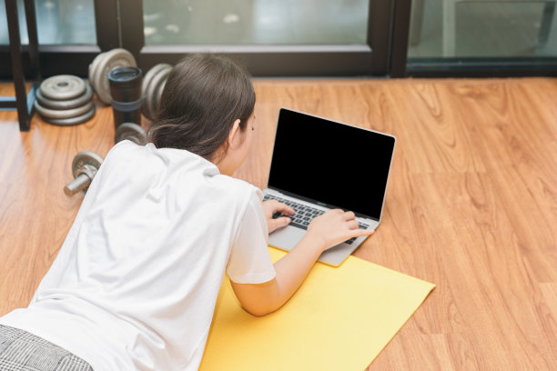 美丽的年轻女子看健身视频教程在笔记本电脑上，而躺在地板上的客厅。图片下载