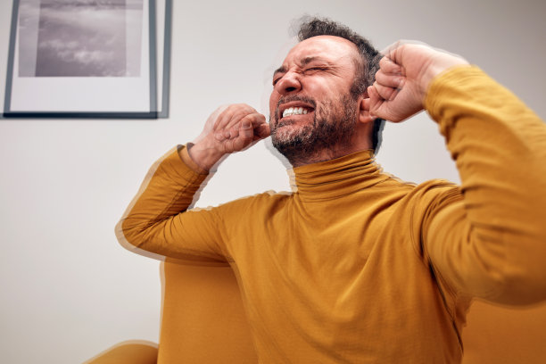 一个成年男子闭上耳朵，脸上露出愤怒的表情。图片下载