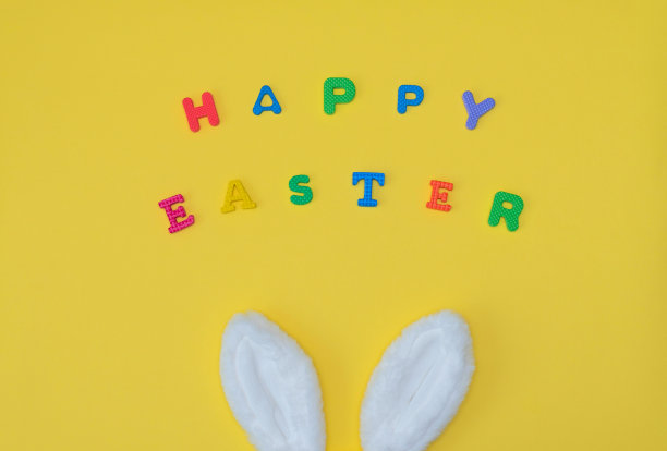 白色复活节兔子耳朵与短语快乐复活节在黄色的背景上明亮的字母。复活节快乐的概念。平面布局风格与复制空间图片下载