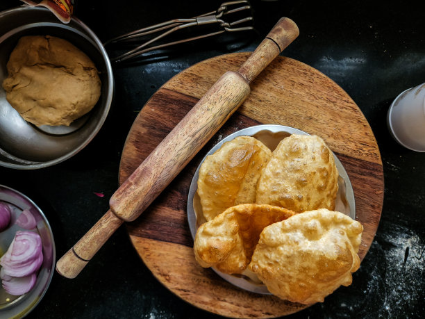 美味的热油炸puri或batura的照片，由小麦粉或所有用途的面粉制成，保存在钢板上。木制滚动板、销子及其他用具的背景。图片下载