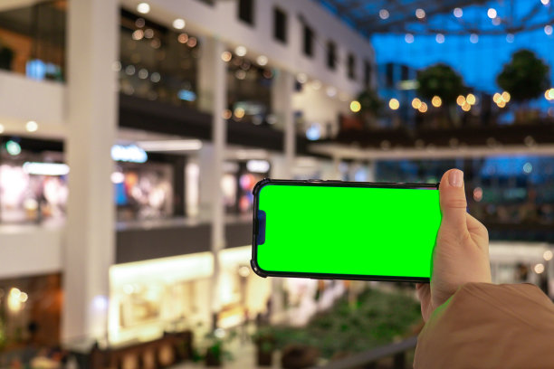 色度键。女人手的特写手持智能手机与绿色屏幕横在商场商店。购物中心。百货商店。网上购物。产品模板图片下载
