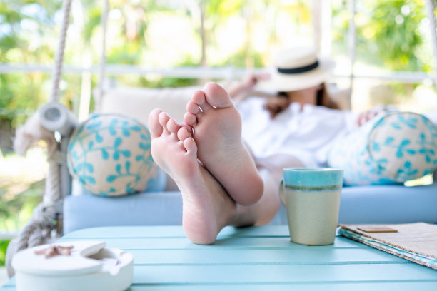 一个年轻的女人用帽子遮住脸，躺在秋千沙发上，桌上放着咖啡杯图片下载