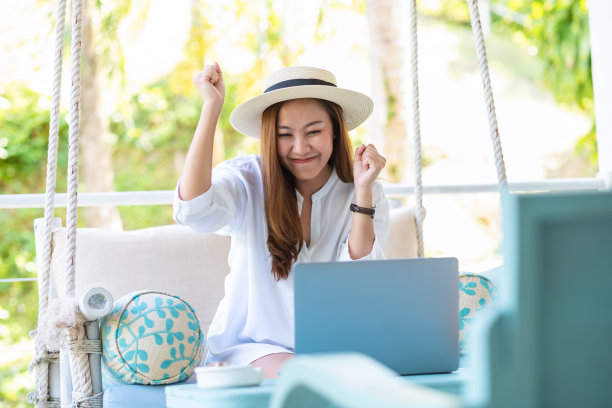 一个激动的年轻亚洲妇女的肖像，举手看着笔记本电脑，享受她的成功图片下载