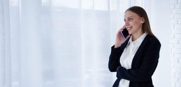 一个快乐的女孩在一个白色的窗户旁打电话谈生意。横幅打印。空间的文本图片下载