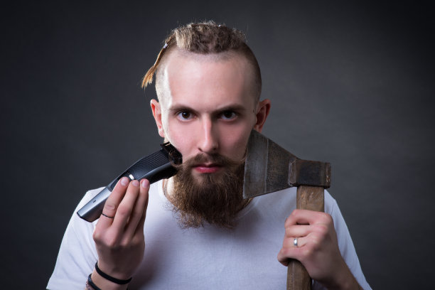 年轻英俊的大胡子男子用剪刀和斧子刮起浓密的胡子图片下载