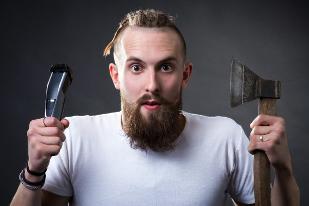 年轻英俊的大胡子男人手里拿着一把斧子和一把剪刀图片下载