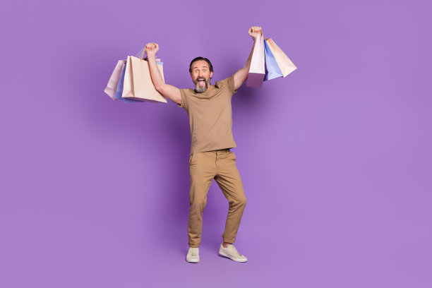 全尺寸照片的老年庆祝男子拿包，穿t恤，裤子，鞋子孤立在紫色的背景图片下载