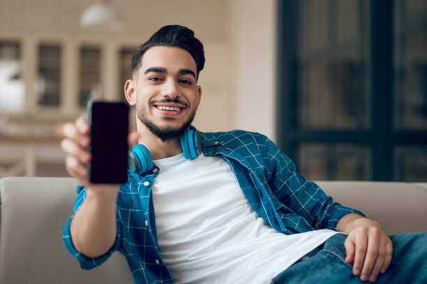 坐在沙发上玩手机的蓝衣青年男人图片下载