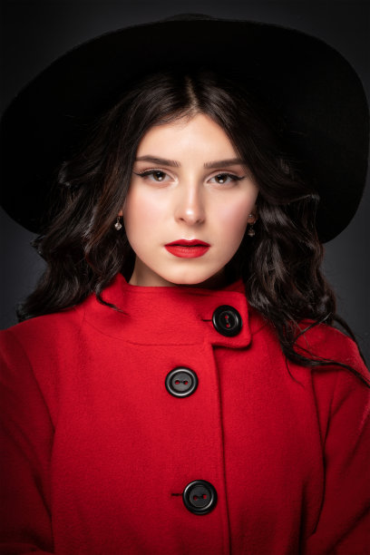 她是一个身材苗条的黑发女人，留着长长的卷发，化着漂亮的妆，穿着一件红色的外套。图片下载