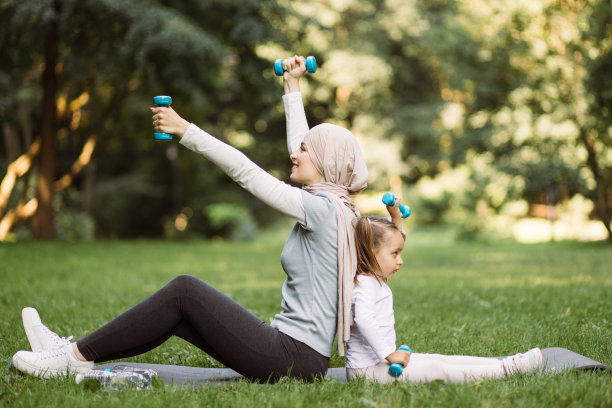 穆斯林母亲和她的女儿，在夏日的新鲜空气中，坐在垫子上举着哑铃图片下载