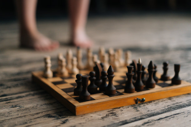 近距离选择性聚焦拍摄赤脚腿的女人站在棋盘附近的木质复古地板在黑暗的房间里，思考着象棋移动。图片下载