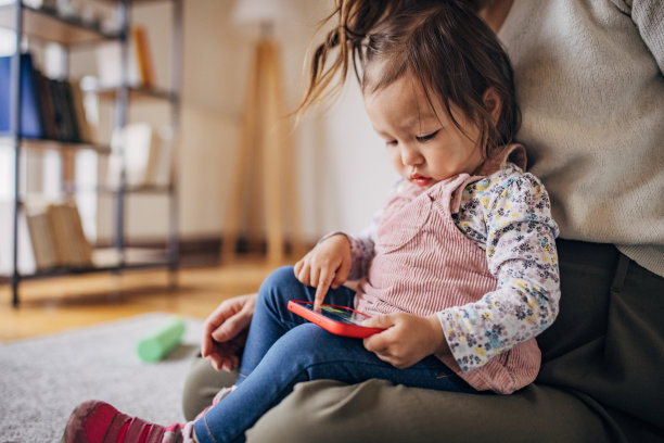 女人坐在地板上和女儿玩，而孩子正在智能手机上看卡通片图片下载