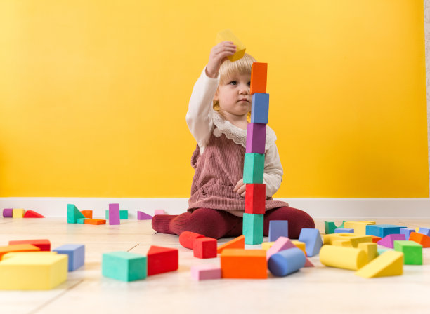 一个专注的小女孩坐在房间的地板上，把一个黄色的立方体放在一个非常高的塔楼上图片下载