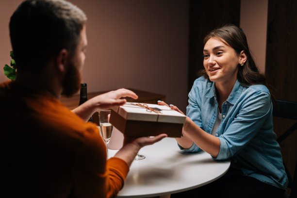 有吸引力的年轻女子在生日或情人节的餐桌上，把包装好的盒子和礼物送给不认识的男人。图片下载