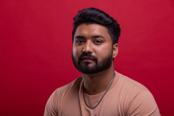 自信，年轻的印度男人的肖像与胡子在红色的背景。图片下载