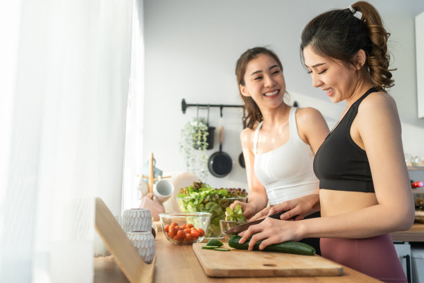 亚洲年轻的两个女子兄妹在厨房里穿着运动服烹饪沙拉。活泼漂亮的女孩妹妹心情愉快，喜欢吃蔬菜，健康饮食，减肥保健在家里图片下载