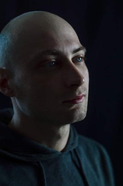 一个英俊的年轻秃顶男子的肖像，他有着蓝色的眼睛，在昏暗的光线下看起来若有所思图片下载
