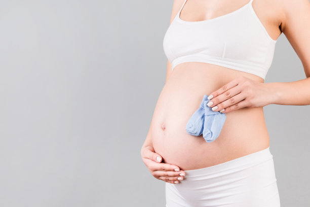 在灰色的背景下，孕妇穿着白色内衣，拿着蓝色袜子，给一个小男孩拍特写。未来儿童期望概念。本空间图片下载