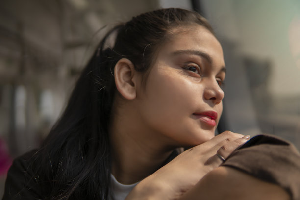 一名年轻女子坐在地铁里，靠窗边思考。图片下载