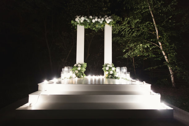 乡村风格的婚礼圆形拱门，装饰着草甸色彩和复古灯泡。在放着花束和蜡烛的木箱旁边。图片下载