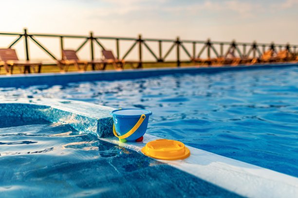 在夏日夕阳的映衬下，池塘的小船上放着一个装满水的儿童水桶和一些玩具图片下载