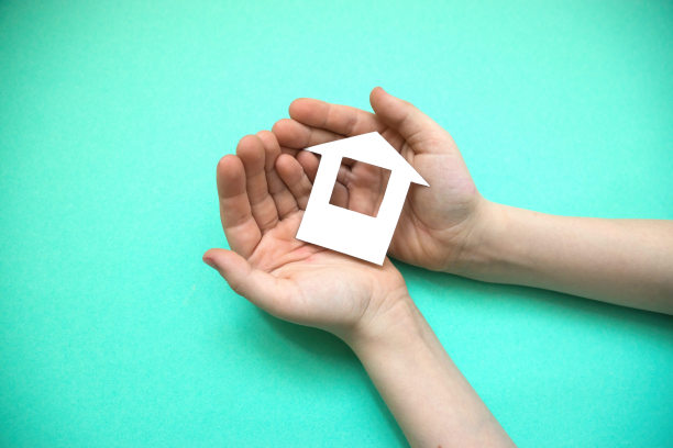 在一个孩子的手里，一幢用纸剪成的房子，背景是浅绿色。孩子们对房子的梦想。儿童和家庭概念公寓。有孩子的家庭按揭主题图片下载