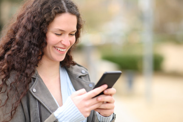 在公园边走边看手机的快乐女人图片下载