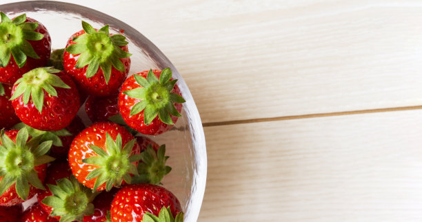 草莓背景材料。桌子上的草莓特写镜头。玻璃碗里的草莓。图片下载