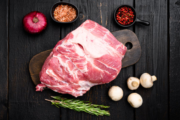 从脖子上取下一块新鲜的生猪肉，配上配料和药草，放在黑色木桌的背景上，俯视图平放图片下载