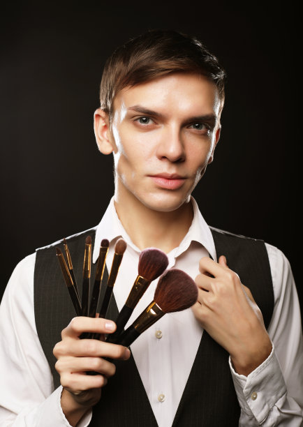 年轻的男性化妆师拿着化妆刷在黑暗的背景上摆造型图片下载