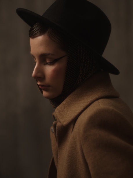 一个美丽的年轻女子在灰色的背景下在工作室里摆姿势。复古外观。秋季或春季外套，黑色帽子和围巾。大眼睛的箭头。图片下载