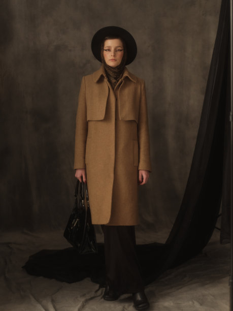 一个美丽的年轻女子在灰色的背景下在工作室里摆姿势。复古外观。秋季或春季外套，黑色帽子和围巾。大眼睛的箭头。图片下载