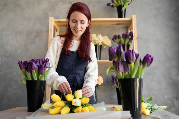 年轻漂亮的女花商在工作围裙收集一束郁金香。图片下载