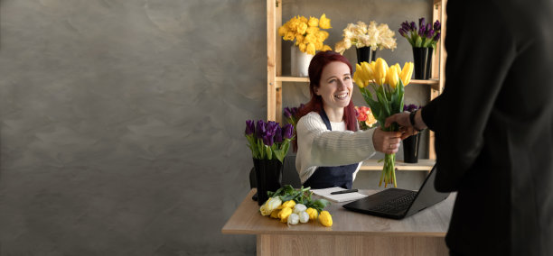 一个年轻人在一家舒适的花店为一个女孩的假期买了一束漂亮的郁金香花。花艺和制作花束在花店。小生意。快乐的卖家。横幅图片下载