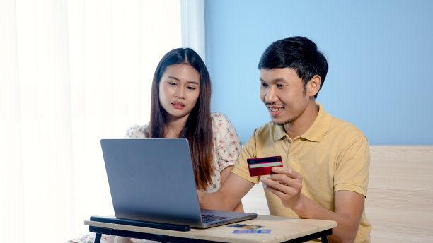 年轻的亚洲男子，一对夫妇正在购物，并通过笔记本电脑在网上订购，两个人选择信用卡支付他们的购买。,网上购物。图片下载