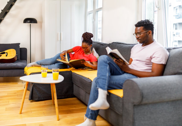 年轻的潮人黑人女性和黑人男性坐在家里客厅的桌子上看书放松。图片下载