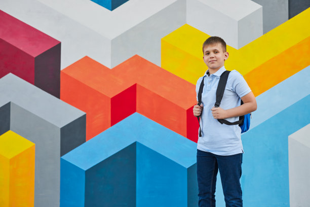 笑眯眯的小男生背着背包靠在五颜六色的墙上图片下载