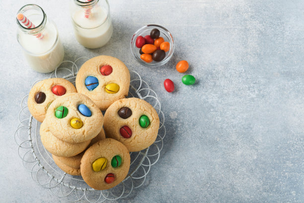 用彩色巧克力糖果和牛奶自制的饼干。浅灰色背景上的奶油酥饼与多色糖果盘与牛奶瓶堆叠。婴儿食品的概念。副本的空间。图片下载