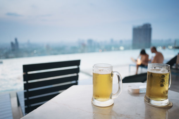 在曼谷的屋顶酒吧享受放松的周五与啤酒在桌子上与泳池的观点图片下载