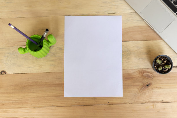 一张空白的A4纸放在一张木制的桌子上，上面放着办公用品图片下载