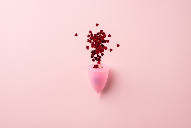 俯视图照片爆炸的红色心脏形状的五彩纸屑从粉红色的月经杯上孤立的淡粉色背景图片下载