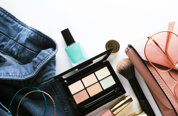 俯视图的女人牛仔裤衬衫，遮瑕膏托盘，唇彩，指甲油，手镯，粉刷在白色背景图片下载