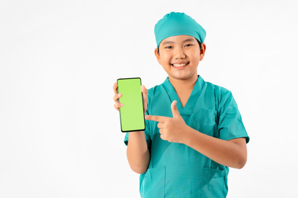 年轻的亚洲男孩的肖像打扮成医生，拿着智能手机与绿色屏幕隔离在白色背景，教育和技术概念图片下载