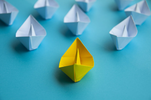 领导概念-黄色纸船折纸领导其余的白色纸船在蓝色封面背景。复制空间概念图片下载