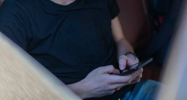 高清照片，一个年轻人坐在汽车的后座上用自己的手机在路上，制定计划，搜索，上网和媒体，聊天，微笑，享受公路旅行在一个美丽的阳光明媚的日子。图片下载