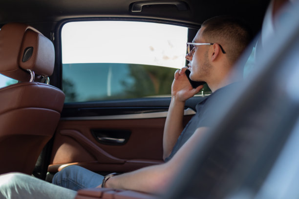 高清照片，一个年轻人坐在汽车的后座上用自己的手机在路上，制定计划，搜索，上网和媒体，聊天，微笑，享受公路旅行在一个美丽的阳光明媚的日子。图片下载