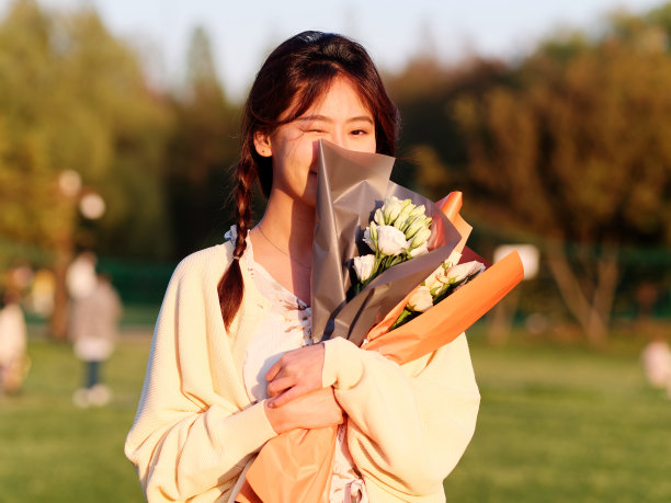 在阳光明媚的日子里，在森林公园里，穿着优雅的中国女孩抱着一束鲜花，享受着无忧无虑的时光。户外时尚肖像魅力年轻的中国开朗的时尚女人图片下载