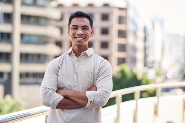一位年轻迷人的亚洲男子双臂交叉站在城市建筑前图片下载