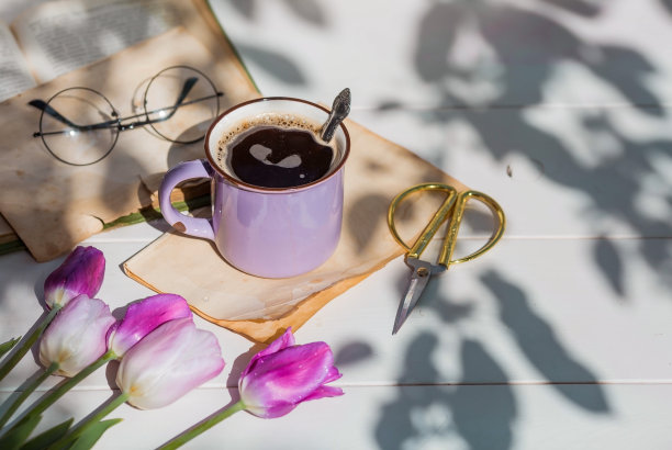 复古风格的静物。一个漂亮的紫色咖啡杯，一本旧书，郁金香和玻璃杯放在木桌上。图片下载