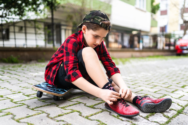 男孩坐在滑板上系鞋带的照片图片下载